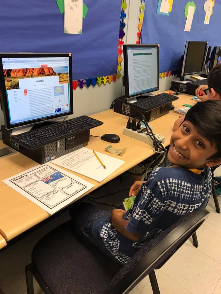 A boy smiling and using computer to research information for essay