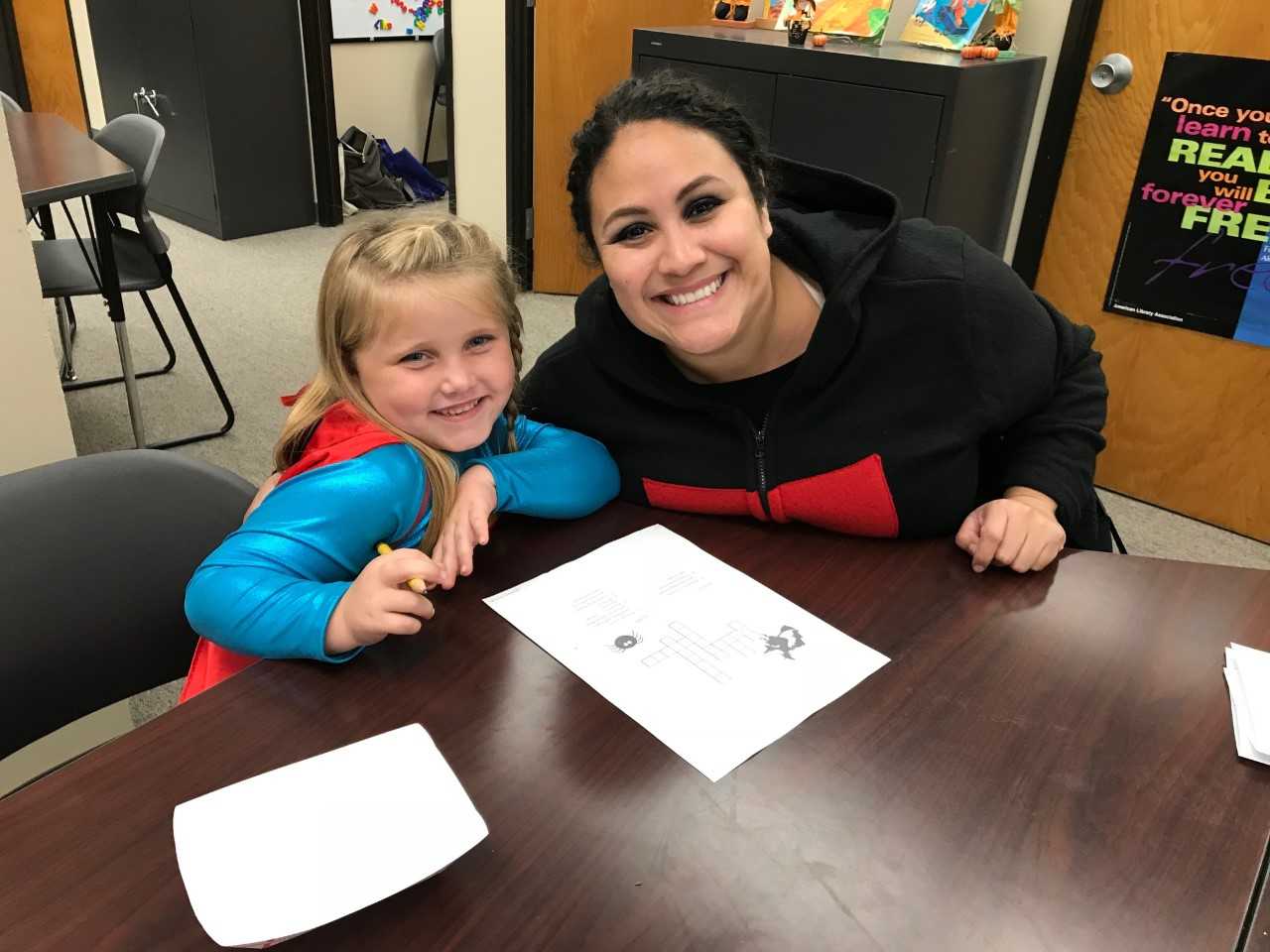 A tutor and a girl smiling and writing a spelling puzzle