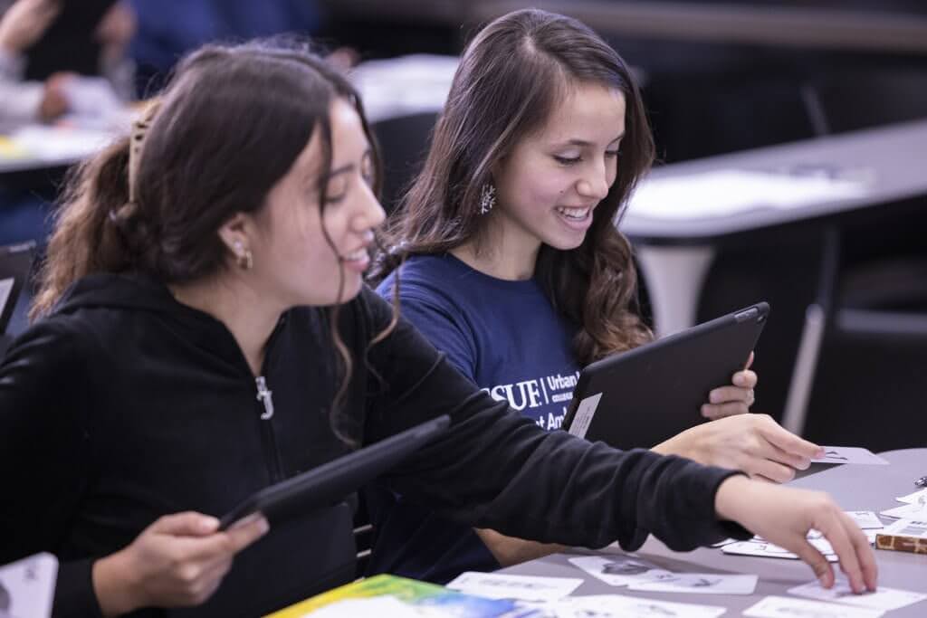 Two smiling college students in a classroom using tablets.